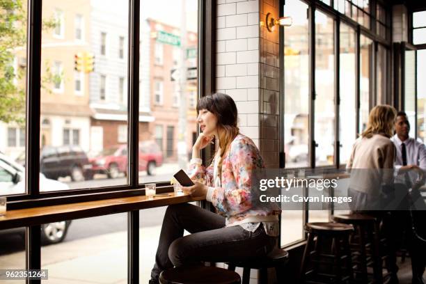 woman holding book while sitting in bar - sgabello foto e immagini stock