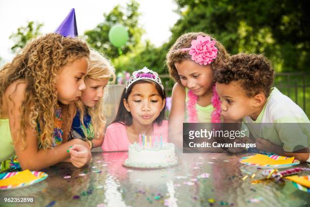 girl blowing birthday cake candles while standing with friends in backyard - vela de cumpleaños fotografías e imágenes de stock