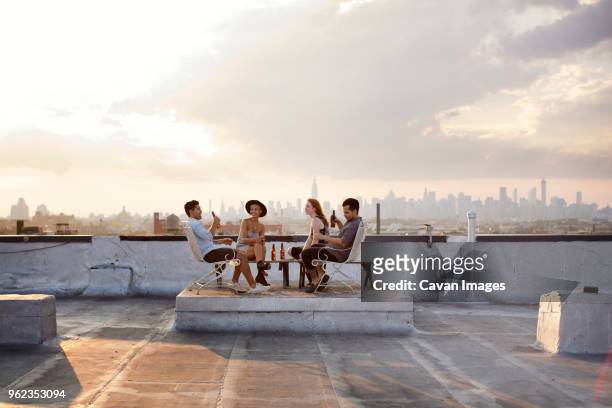 happy friends enjoying while having beer at building terrace during sunset - four people stock-fotos und bilder