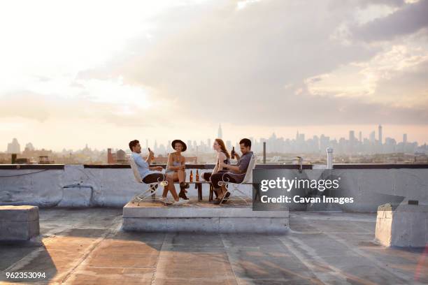 happy friends enjoying while having beer at building terrace during sunset - european outdoor urban walls stockfoto's en -beelden