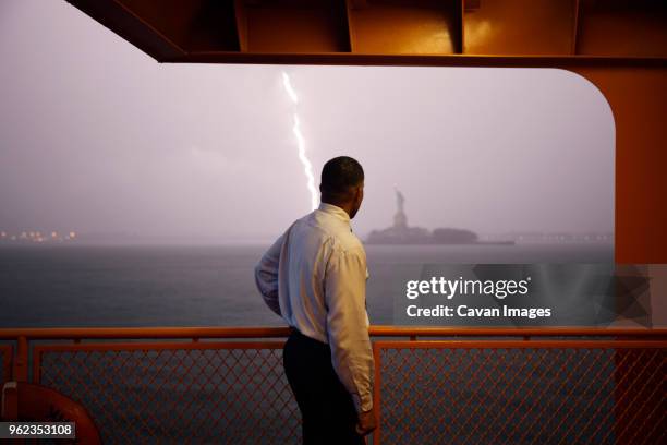 businessman looking at statue of liberty while standing by railing on ferry during stormy weather - liberty eiland stockfoto's en -beelden