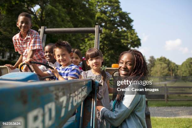 portrait of teacher with children by tractor on field - portrait of school children and female teacher in field stock pictures, royalty-free photos & images