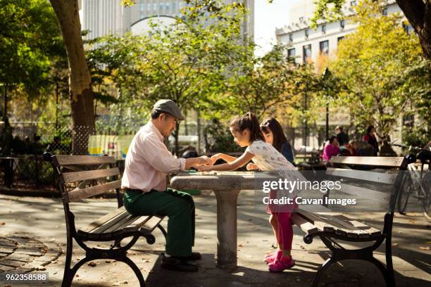 side view of girls playing checkers game with grandfather at table in park - 2014 asian games stock-fotos und bilder