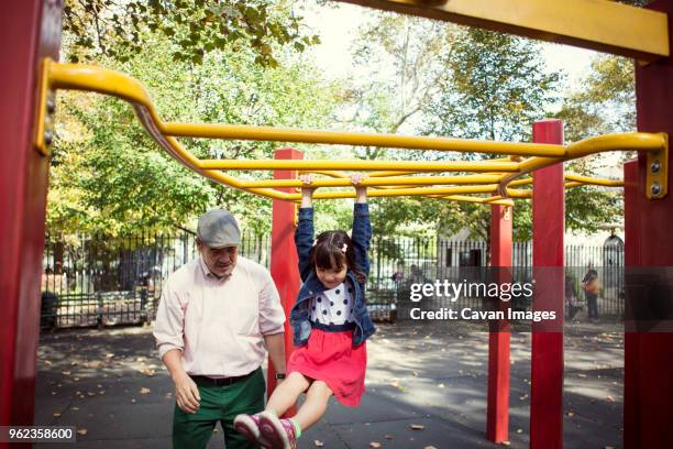 grandfather looking at granddaughter hanging on jungle gym in park - jungle gym ストックフォトと画像