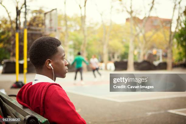 thoughtful student listening music while sitting on bench at basketball court - student day dreaming stock pictures, royalty-free photos & images