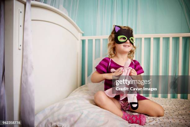 cute girl wearing mask playing with doll while sitting in crib - doll house stockfoto's en -beelden