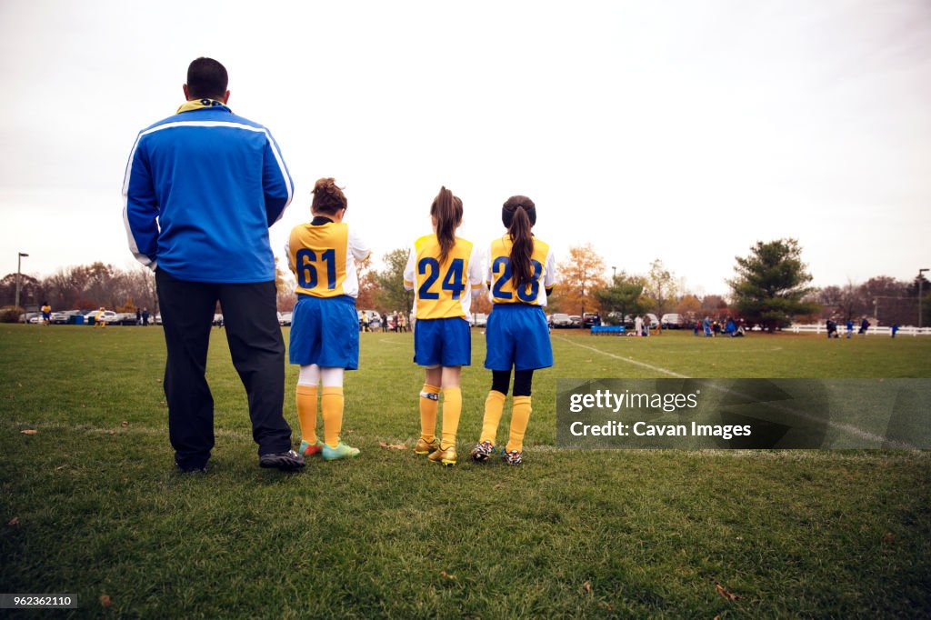 Rear view of soccer players standing with coach on playing field