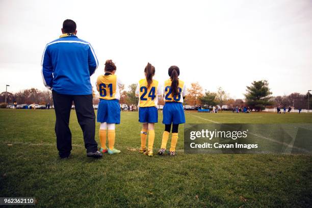 rear view of soccer players standing with coach on playing field - soccer team coach stock pictures, royalty-free photos & images