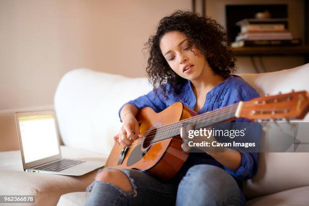 woman practicing guitar while sitting on sofa at home - woman playing guitar stock pictures, royalty-free photos & images