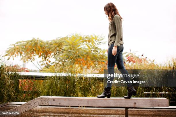 full length of woman walking on railing by plants against clear sky - females walking stock pictures, royalty-free photos & images