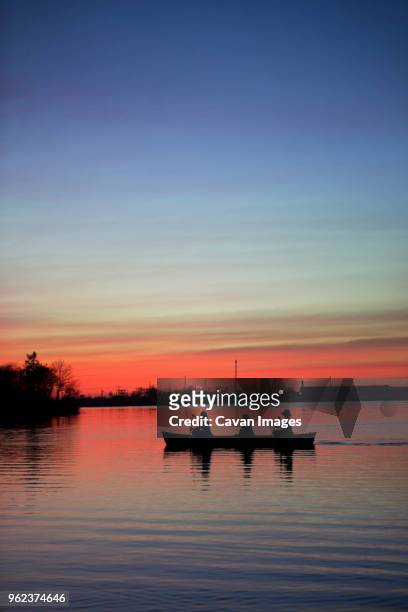 silhouette friends rowing boat on lake against sky during sunset - blue sky friends photos et images de collection