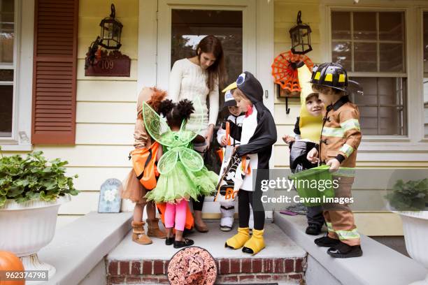 woman distributing candies to children in halloween costumes during trick or treating - dolcetto o scherzetto foto e immagini stock