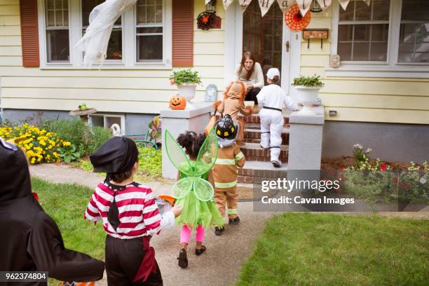 children in halloween costumes walking towards woman during trick or treating - boy fireman costume stock pictures, royalty-free photos & images