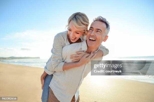 coppia matura che gioca sulla spiaggia al tramonto o all'alba. - man hugging woman foto e immagini stock