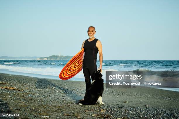 senior surfer at beach with dog - man surfing photos et images de collection