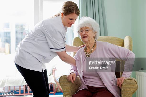 nurse helping senior woman to her feet in care home - huishoudelijke dienstverlening stockfoto's en -beelden