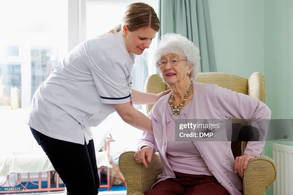 Nurse helping senior woman to her feet in care home