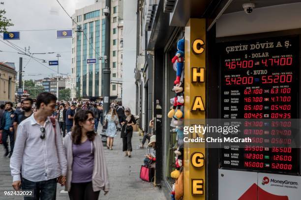 People walk past a currency exchange office showing the rates for USD and Euros against the Turkish Lira on Istanbul's famous Istiklal shopping...