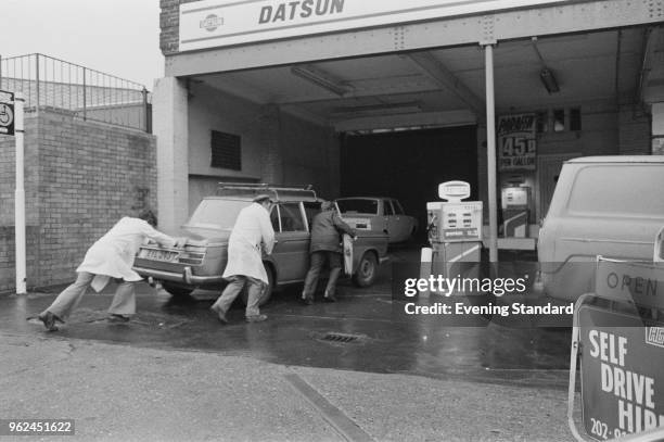 Gas jockeys helping a man to push his car near the petrol pump to refuel, London, UK, 27th December 1978.