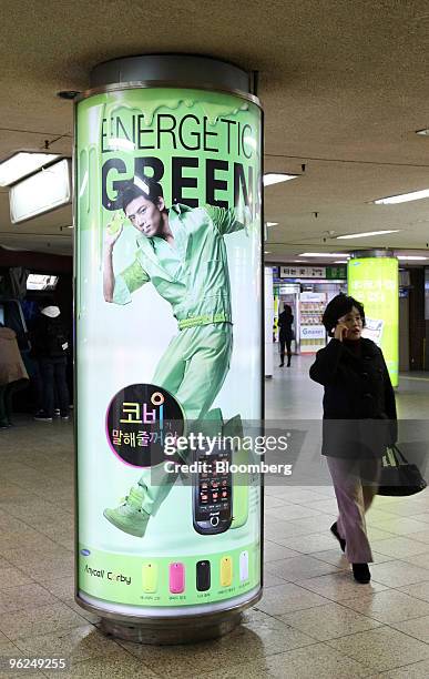 Woman using her mobile phone walks past an advertisement for Samsung Electronics Co.'s Anycall brand of mobile phones at Gang-Nam subway station in...