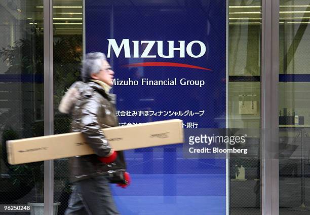 Pedestrian walks past a sign for Mizuho Financial Group Inc. Outside the bank's headquarters in Tokyo, Japan, on Friday, Jan. 29, 2010. Mizuho...
