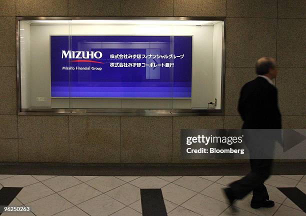 Man walks past a sign for Mizuho Financial Group Inc. Outside the bank's headquarters in Tokyo, Japan, on Friday, Jan. 29, 2010. Mizuho Financial...