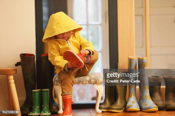 young child putting on wellington boots - hood clothing stock pictures, royalty-free photos & images