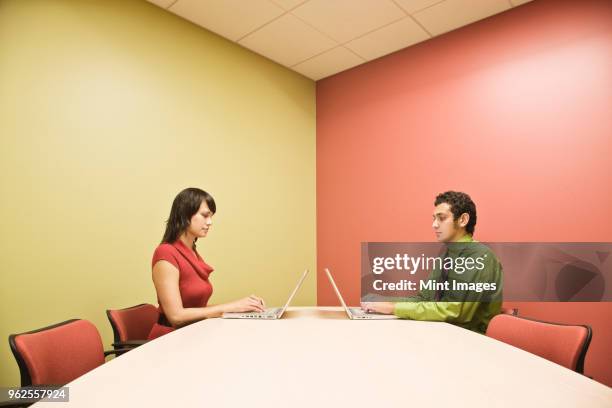 hispanic man and caucasian woman on lap top computers in a colourful office conference room. - woman sitting top man stock pictures, royalty-free photos & images