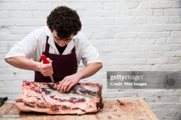 man wearing apron standing at a wooden butchers block, butchering beef forerib. - wooden block stockfoto's en -beelden