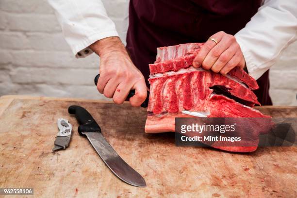close up of butcher wearing apron standing at a wooden butchers block, butchering piece of pork loin. - knife block stock-fotos und bilder
