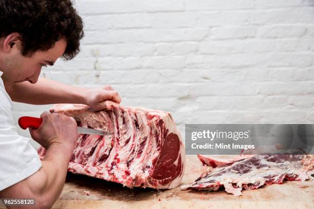 close up of man wearing apron standing at a wooden butchers block, butchering beef forerib. - wooden block stockfoto's en -beelden