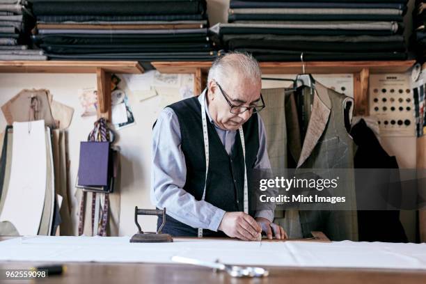 tailor with measuring tape around neck working with material at bench - tailor stock pictures, royalty-free photos & images