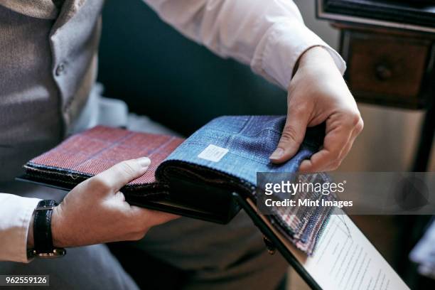 a tailor looking at fabric samples in a book, tweed and wool for mens clothes. - tailor stock pictures, royalty-free photos & images