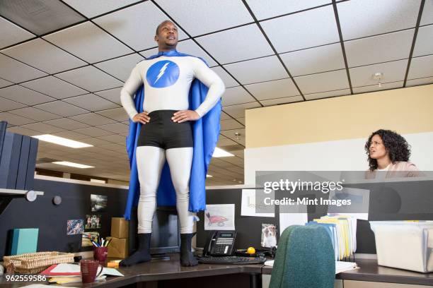 a black businessman office super hero stands on his cubicle desk ready for action. - physical position fotografías e imágenes de stock