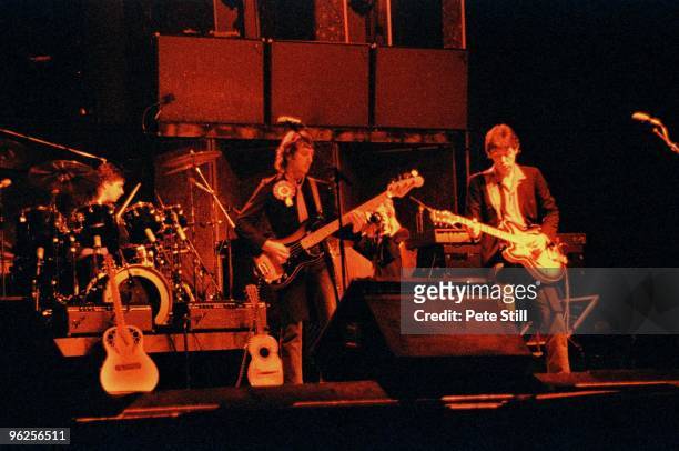 Steve Holly, Denny Laine and Paul McCartney of Wings perform on stage while photographer wife Linda McCartney takes pictures in the background, at...