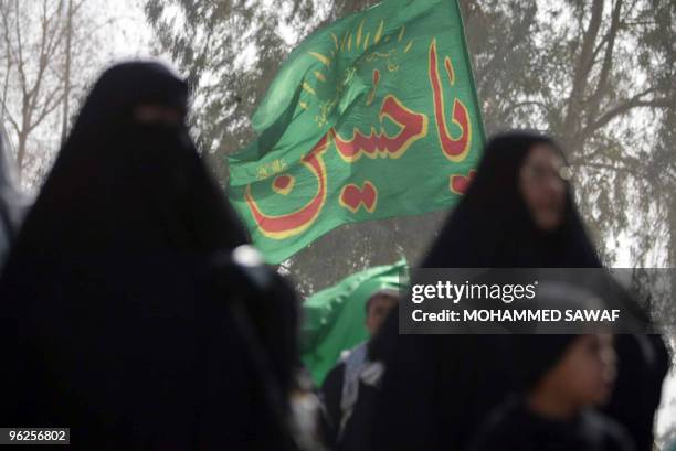 Shiite Muslim pilgrims walk past green banners bearing the name of Prophet Mohammad's grandson, Imam Hussein, on the raod between the holy cities of...