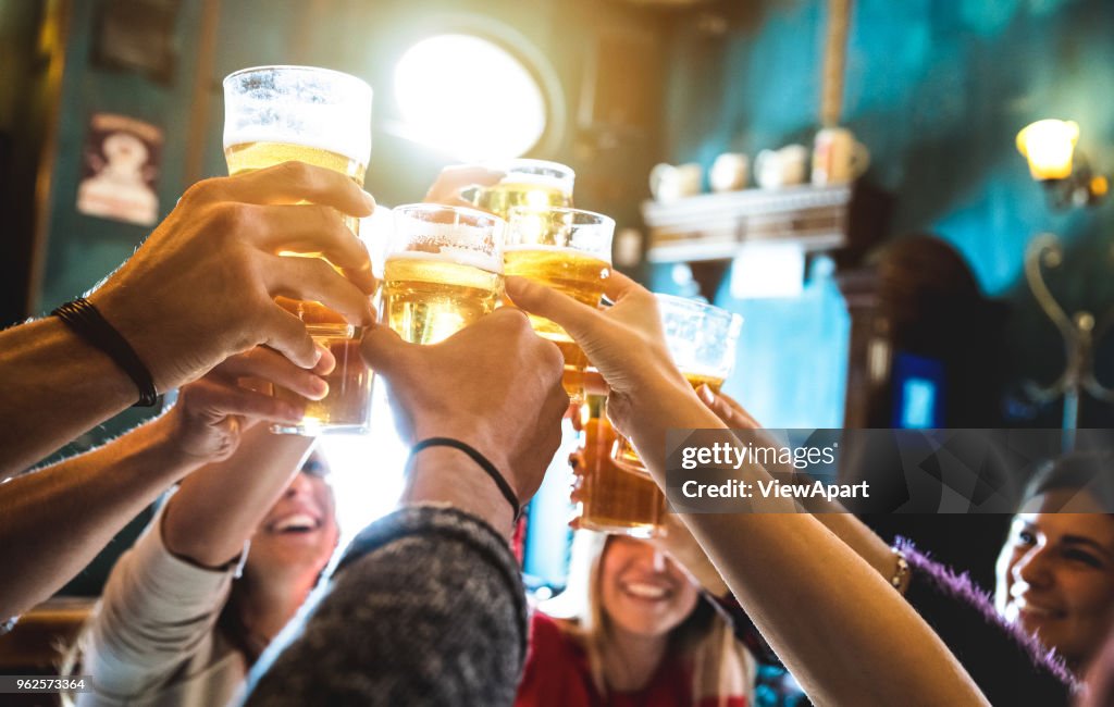Grupo de amigos felices bebiendo y tostado de la cerveza en la cervecería restaurante bar - concepto de amistad con los jóvenes que se divierten juntos en el pub vintage cool - enfoque en vaso de cerveza medio - imagen iso alta