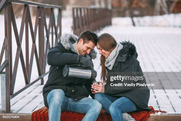 happy man pouring drink from insulated container on boardwalk during winter - insulated drink container foto e immagini stock