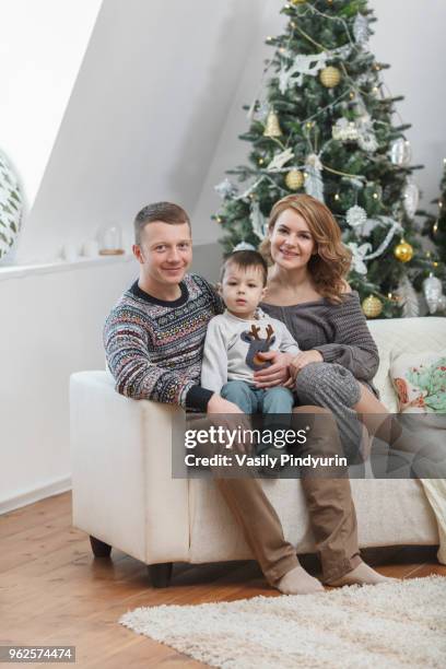 portrait of smiling father and mother sitting with son on sofa against christmas tree at home - pindyurin foto e immagini stock