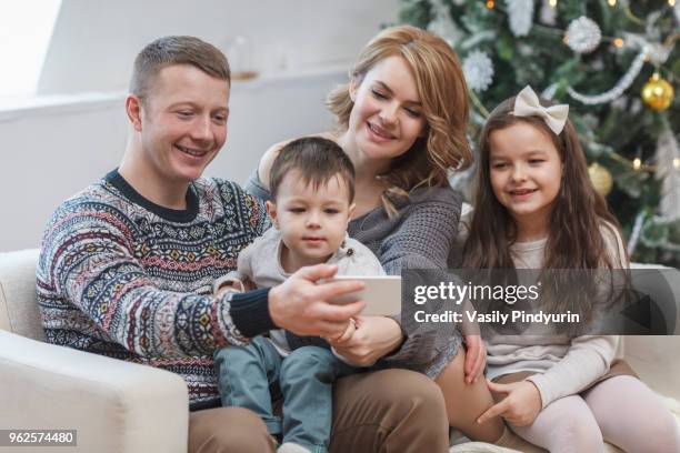 happy man sharing mobile phone with family on sofa at home during christmas - pindyurin stock-fotos und bilder