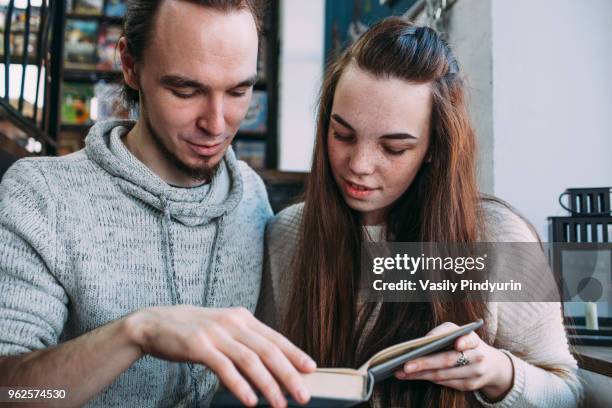 young couple reading book while sitting at cafe - pindyurin stock-fotos und bilder