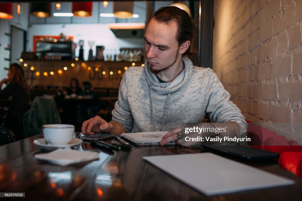 Young man using mobile phone while sitting with book on table at cafe