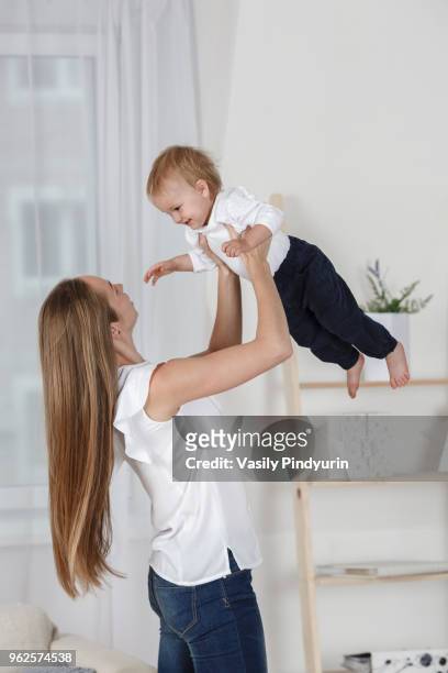 happy mother holding daughter aloft at home - pindyurin stock-fotos und bilder