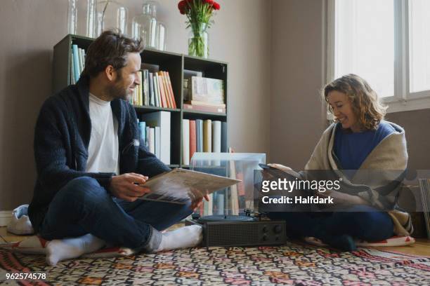 happy mid adult couple sitting with records by turntable on carpet at home - woman in a shawl stock pictures, royalty-free photos & images