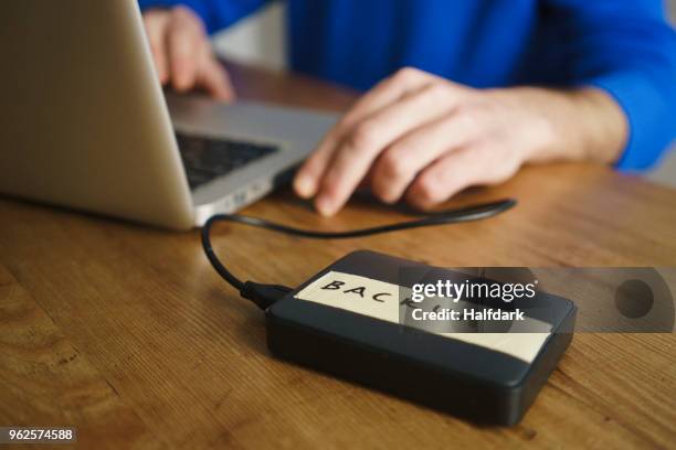 midsection of man using laptop with backup label on external hard disk drive at table - backup foto e immagini stock