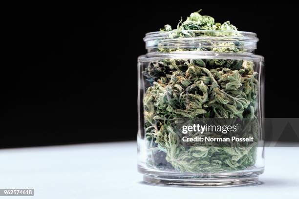 marijuana leaves in glass jar on table against black background - marijuana herbal cannabis stockfoto's en -beelden