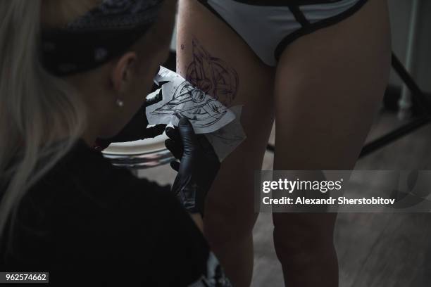 artist peeling off tattoo stencil on female customer's thigh at studio - peeling off bildbanksfoton och bilder