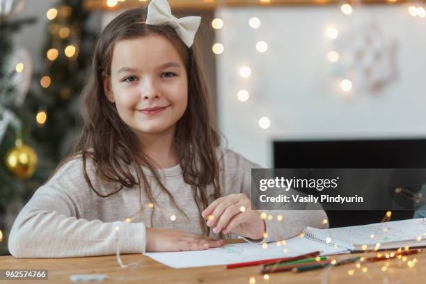 portrait of smiling girl sitting at table with illuminated string lights - pindyurin stock-fotos und bilder