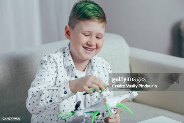 smiling boy adjusting drone while sitting on sofa at home - pindyurin stock-fotos und bilder