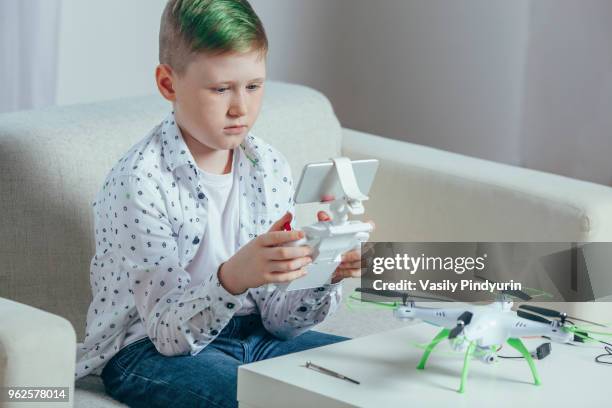 boy using remote control sitting on sofa by drone on coffee table at home - pindyurin foto e immagini stock